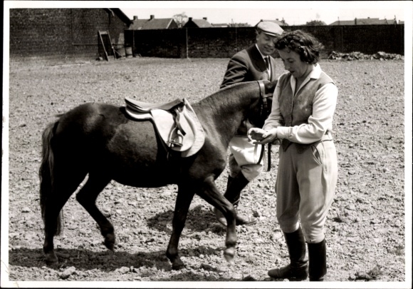 Foto Mann führt ein gesatteltes Pony, Frau in Reitkleidung